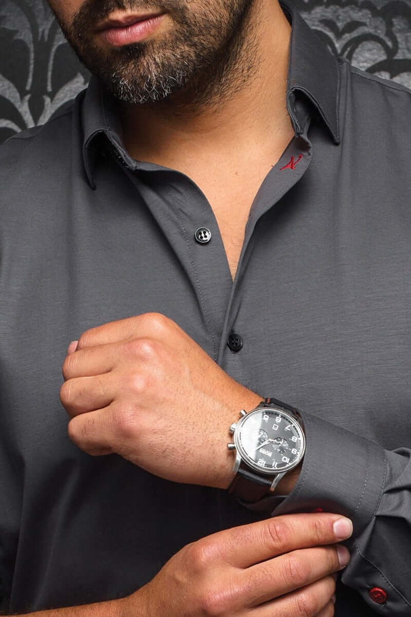 Homme portant une chemise grise élégante avec boutons noirs et détails rouges, montrant une montre élégante.