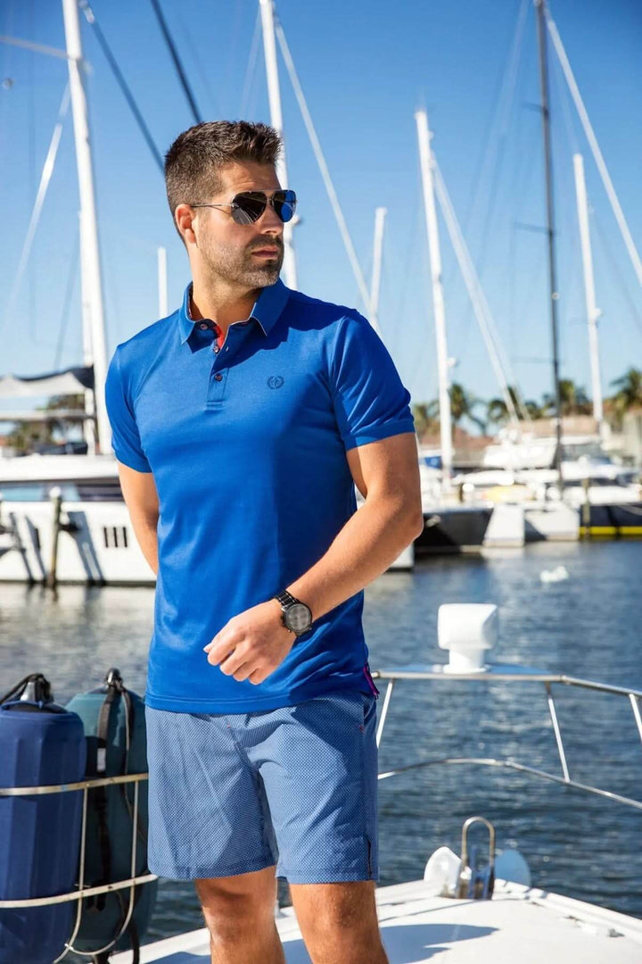 Homme en polo bleu sur un yacht, combinant style sport et élégance en bord de mer.
