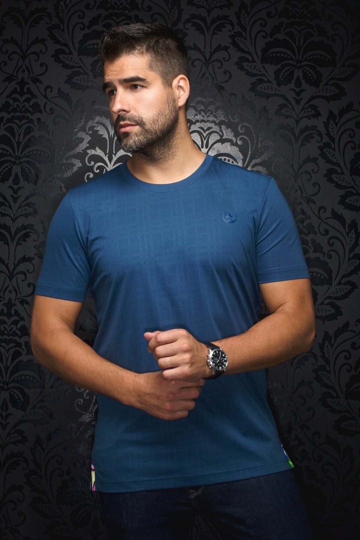 Homme portant un t-shirt bleu moderne avec col rond et motif ton sur ton, idéal pour un look urbain chic.