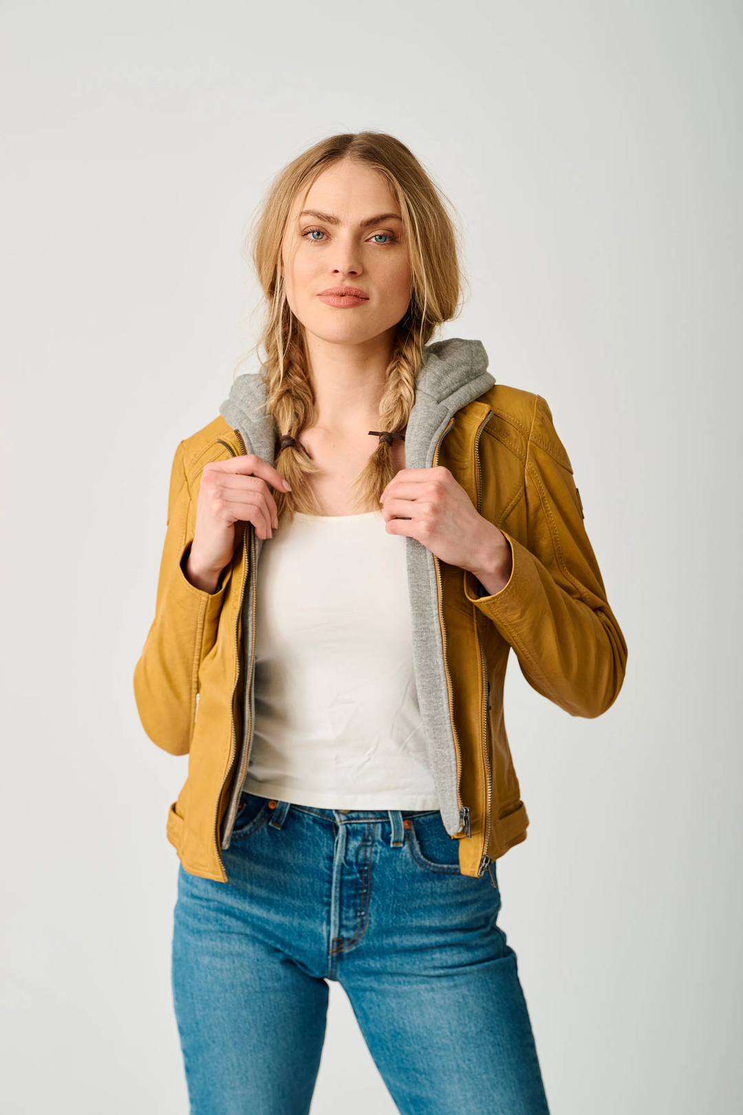 Femme portant la Veste Allice en cuir véritable avec capuche amovible, style urbain et coupe ajustée, couleur jaune moutarde.