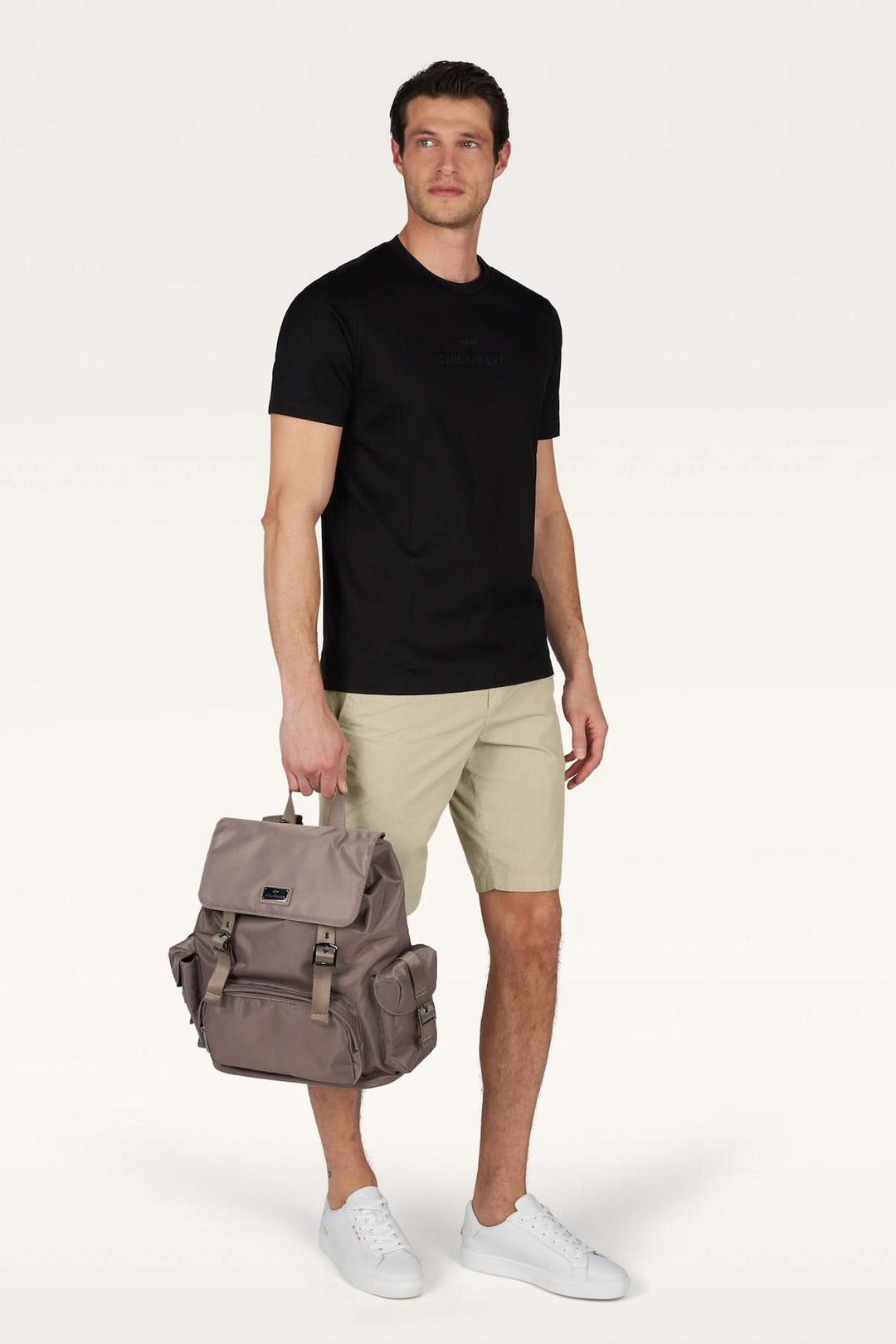 Homme portant un Bermuda en popeline de coton ultralégère beige avec t-shirt noir et sac à dos gris, prêt pour une journée décontractée.