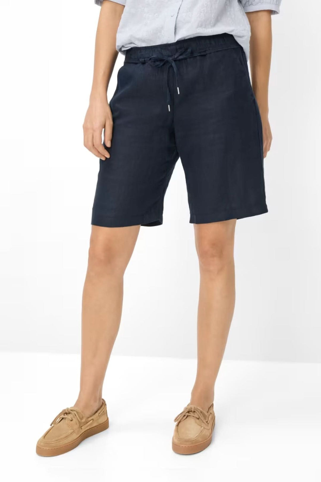 Femme portant des Bermudas en lin MEL B avec une chemise et des sandales, présentant un look décontracté sophistiqué.