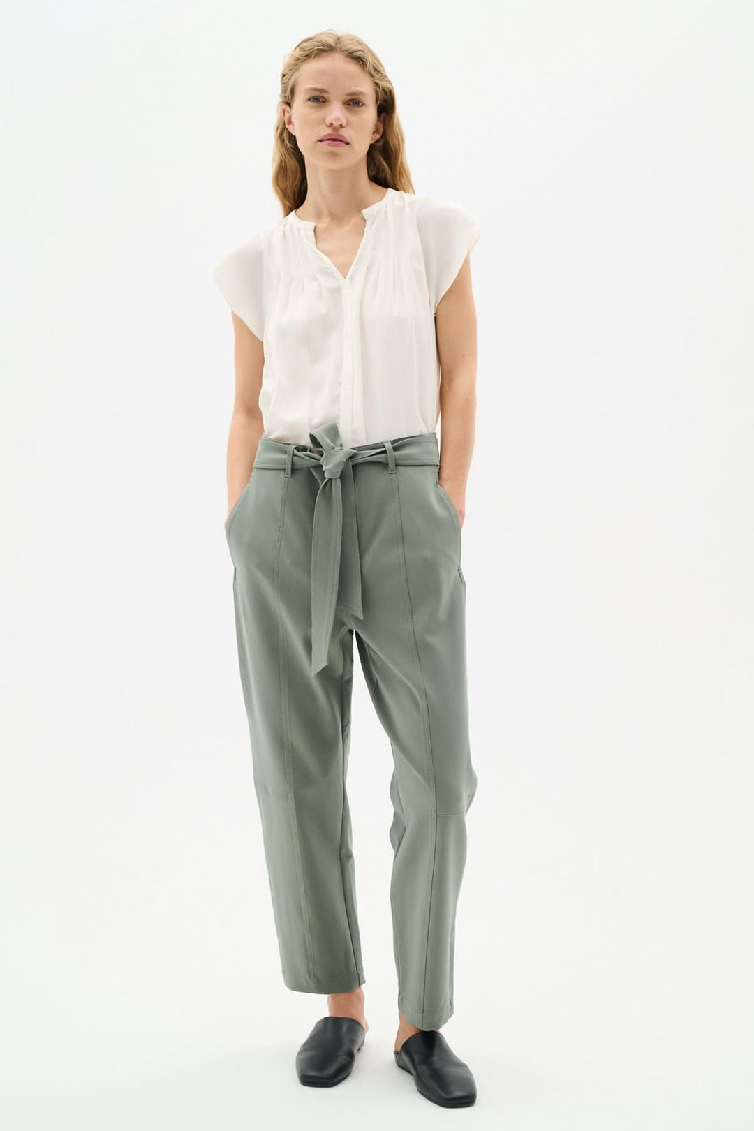 Femme portant une blouse blanches légère et des pantalons verts, avec un style élégant et décontracté.