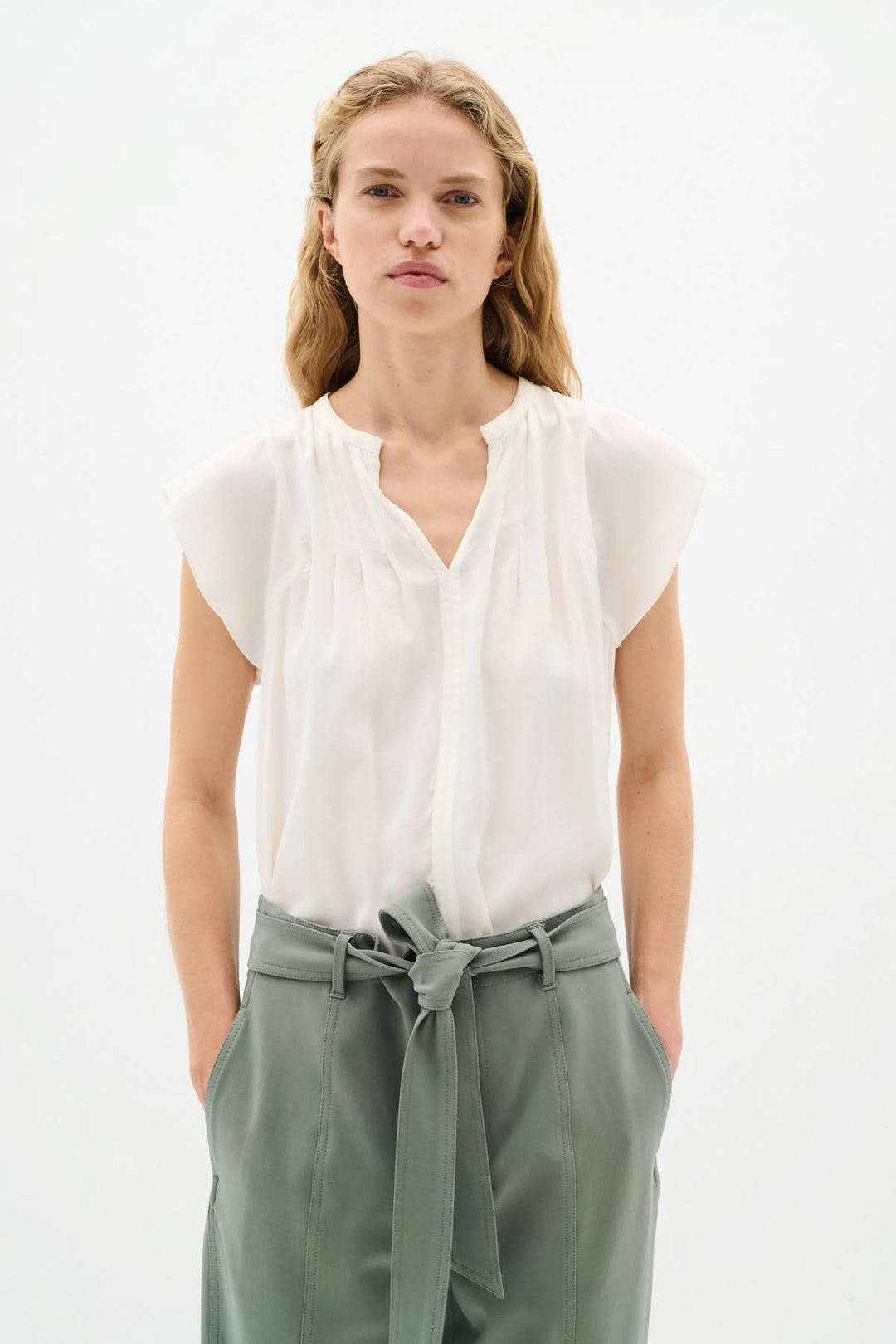 Blouse Cidenza blanche légère avec encolure plissée et manches volantes, portée avec un pantalon vert.