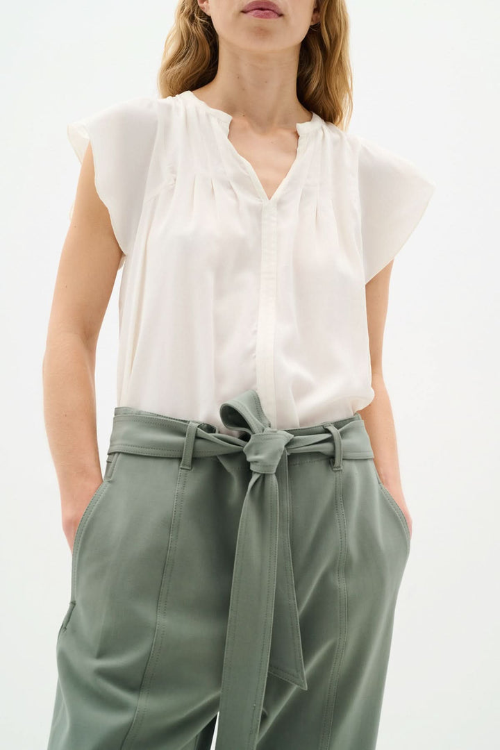 Blouse légère Cidenza à encolure plissée et manches volantes, portée avec un pantalon noué.