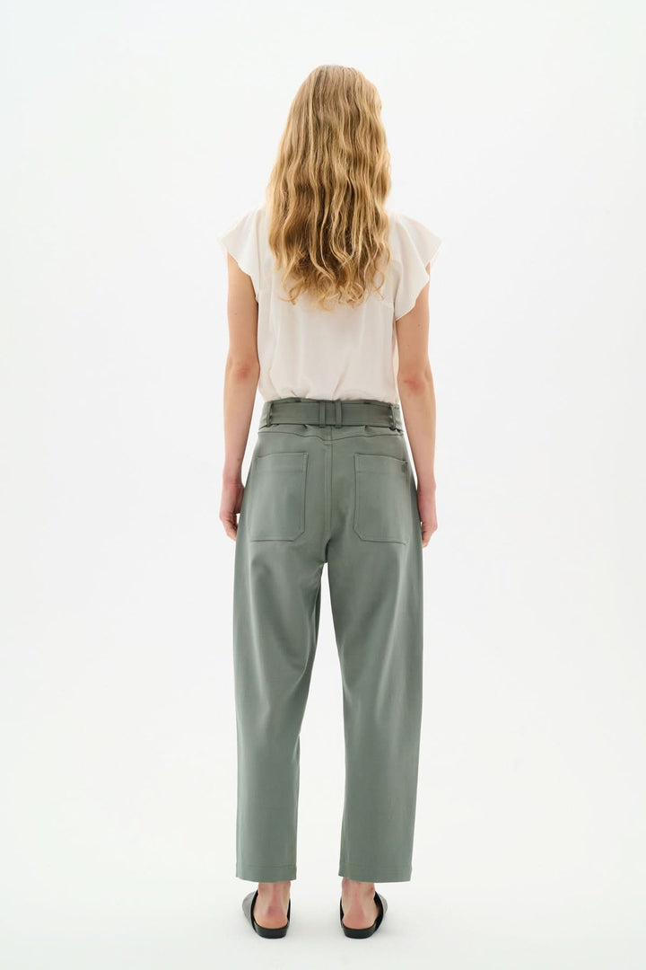 Femme vue de dos portant une blouse légère crème et un pantalon élégant en vert pastel.