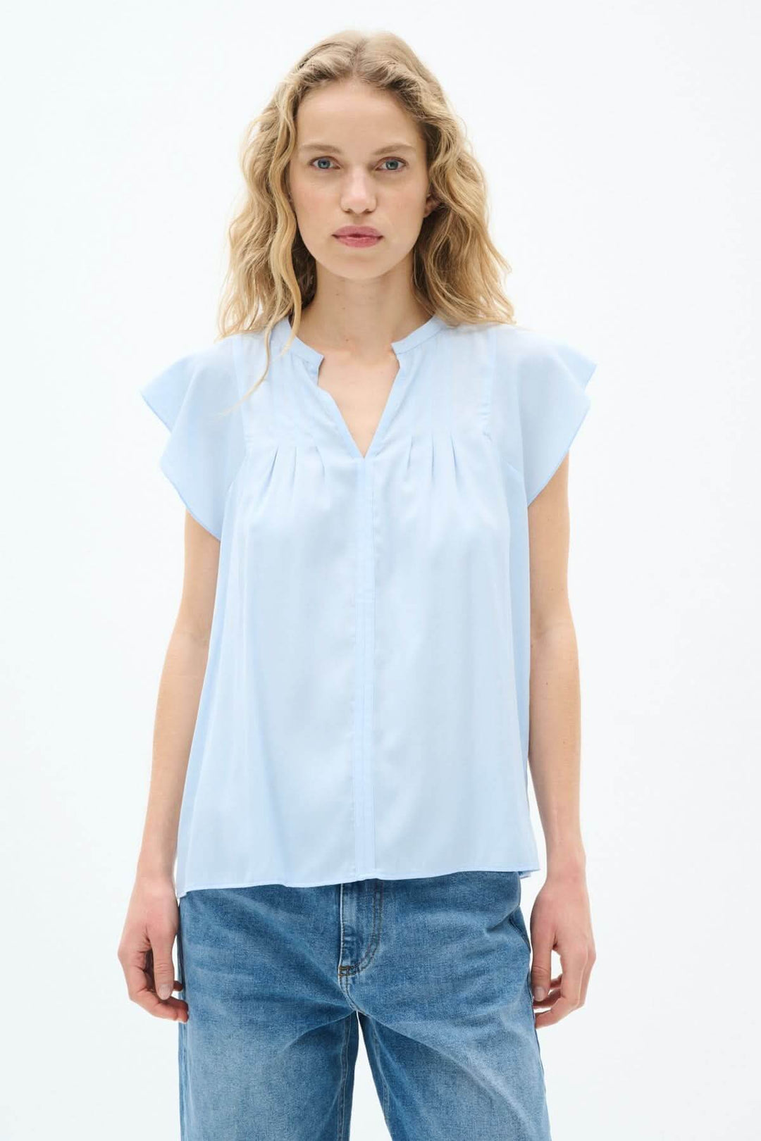 Blouse légère Cidenza en bleu clair avec encolure plissée et manches volantes, style féminin et élégant.