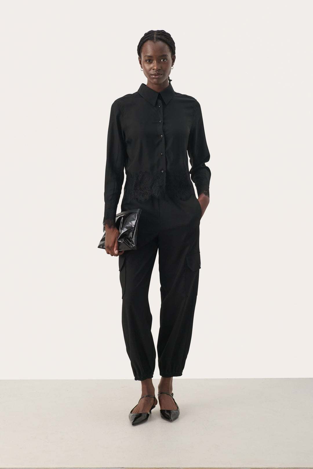 Femme portant une blouse noire élégante avec manches longues, pantalon coordonné et clutch, look chic et sophistiqué.
