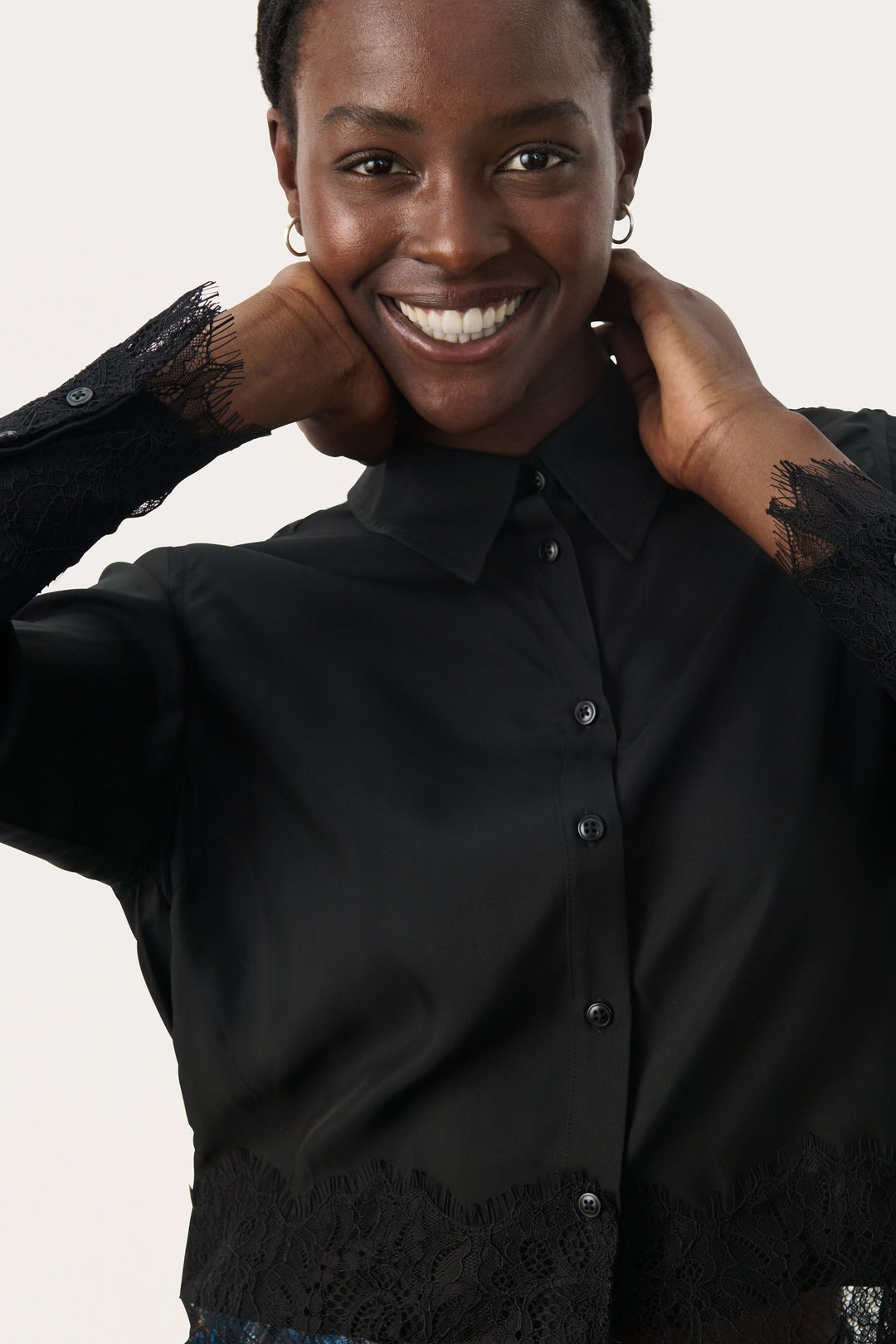 Femme souriante portant une blouse noire élégante avec des manches en dentelle, parfaite pour toutes occasions.