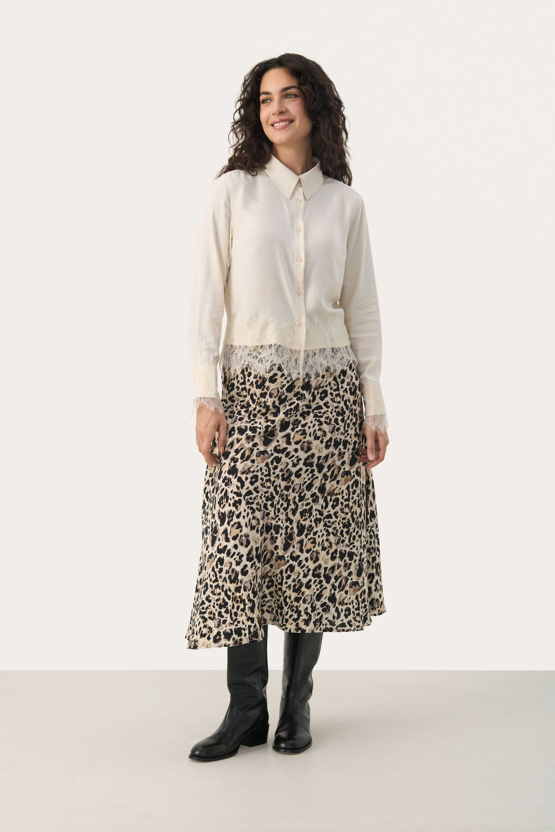 Femme portant une blouse Lenina élégante avec dentelle, associée à une jupe léopard longue et des bottes noires.