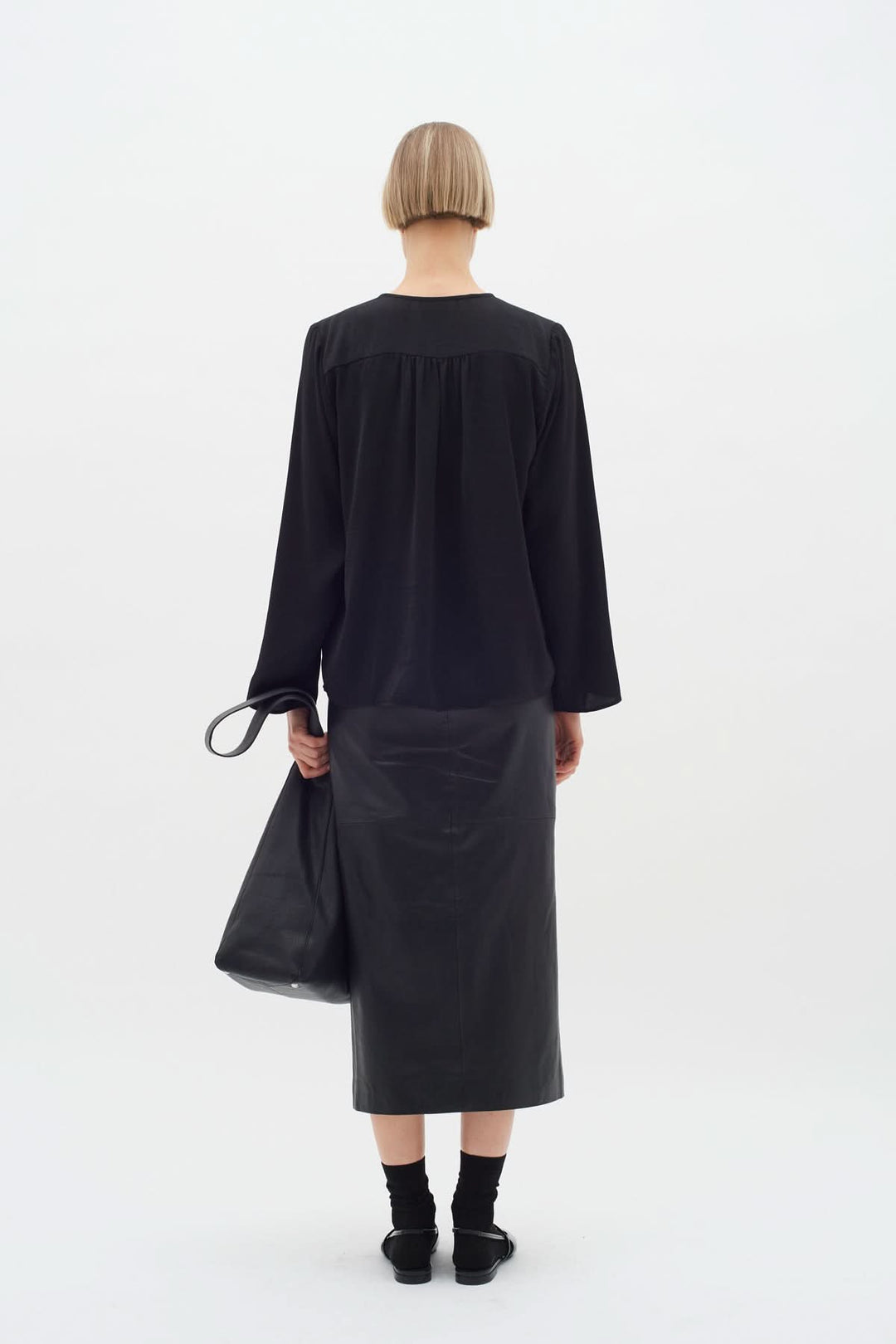 Femme portant une blouse noire avec une jupe en cuir, vue de dos, style élégant et moderne.