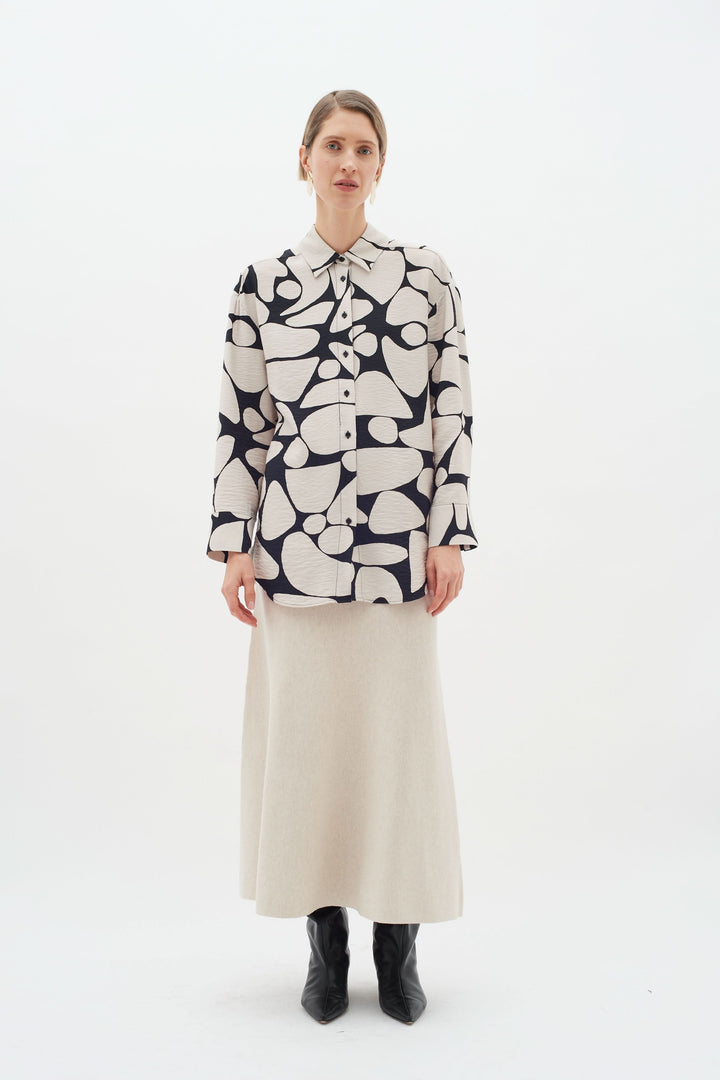 Blouse Metta à col classique, imprimé abstrait, portée avec une jupe longue et des bottines, look élégant.