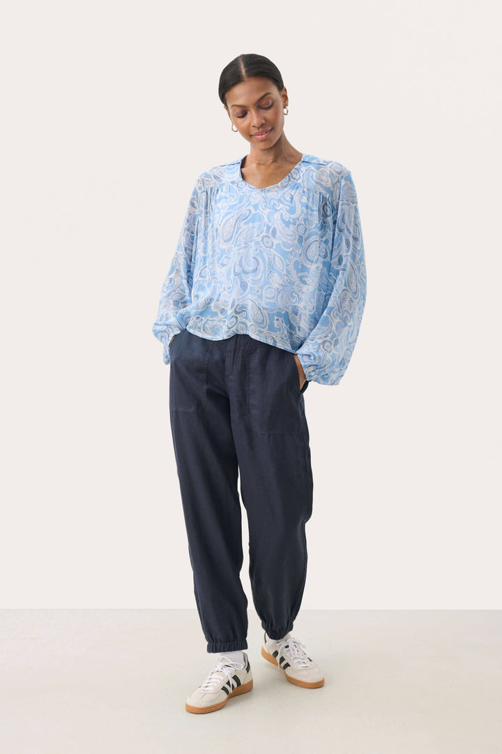 Femme portant une blouse légère en viscose bleue avec imprimé paisley et un pantalon noir décontracté.