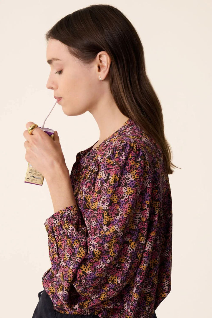Femme portant une blouse Tamtam colorée, dégustant une boisson avec une paille.