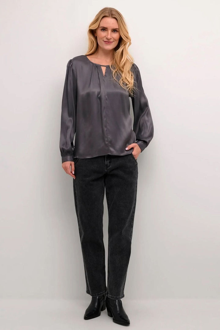 Blouse Viria grise à manches longues avec col en goutte d'eau, portée avec un pantalon noir, élégante et chic.