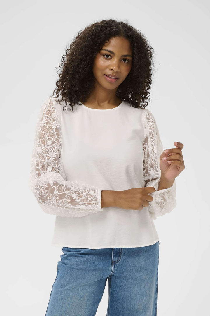 Blouse avec broderie en dentelle avec manches longues portées par une femme, idéale pour un look élégant et raffiné.