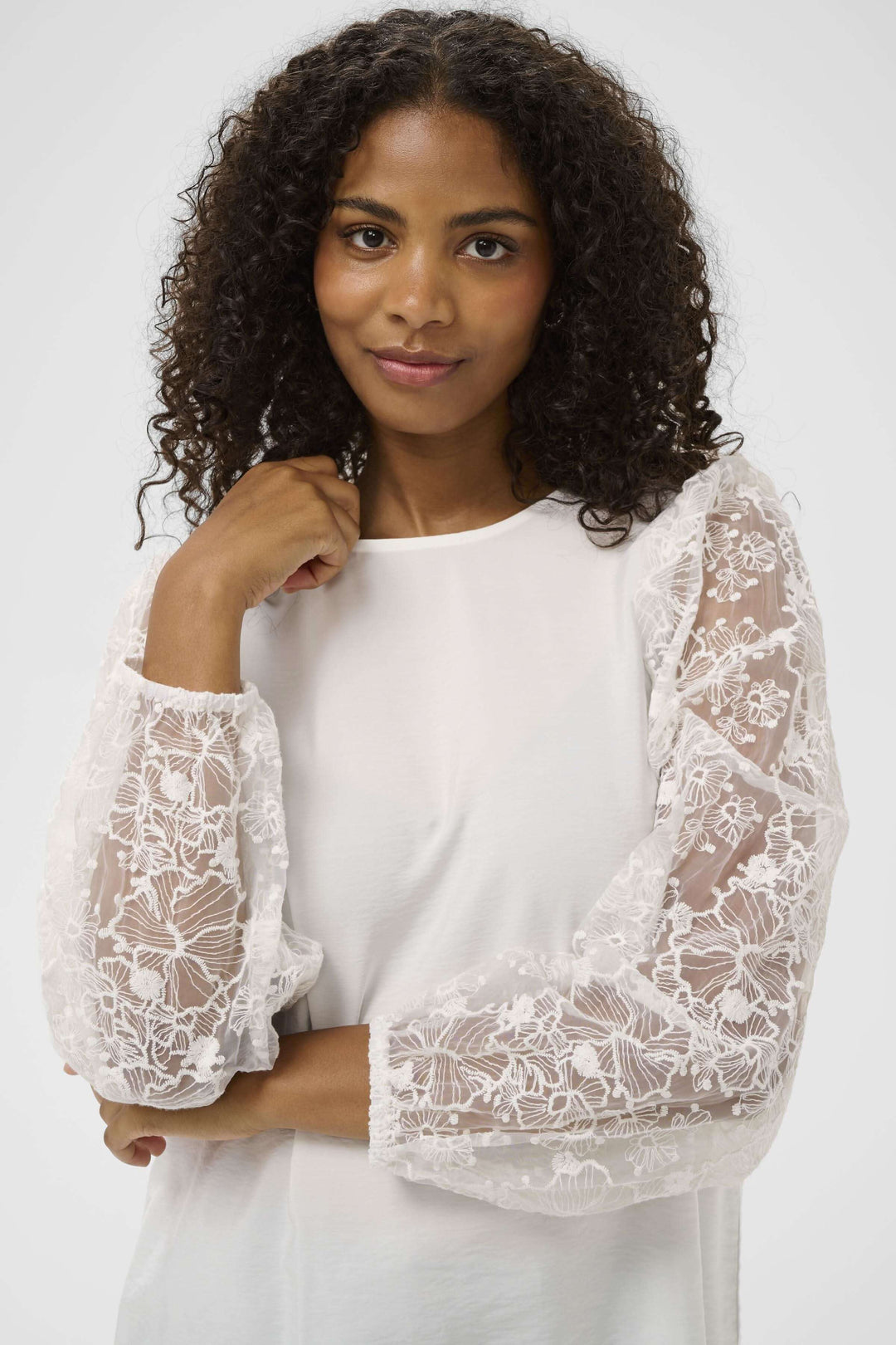 Blouse avec broderie avec manches longues en dentelle, silhouette féminine et élégante, portée par une femme souriante.