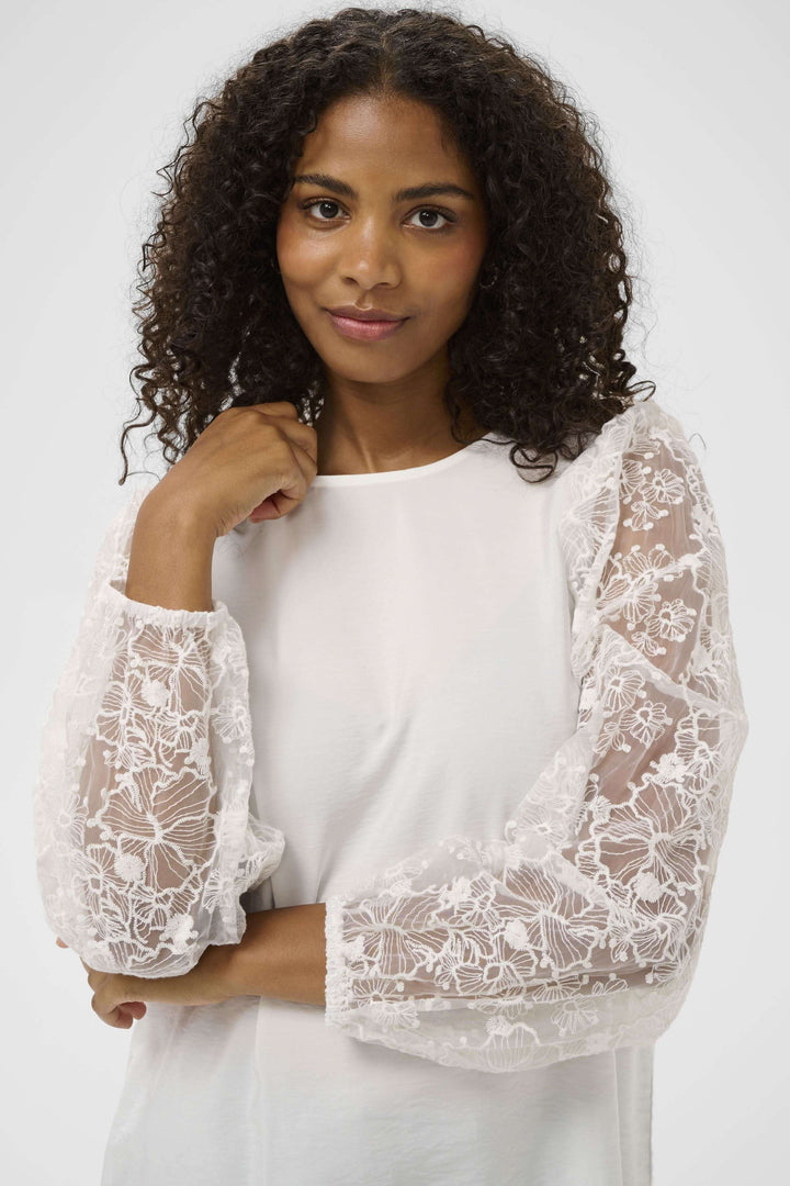 Blouse avec broderie avec manches longues en dentelle, silhouette féminine et élégante, portée par une femme souriante.