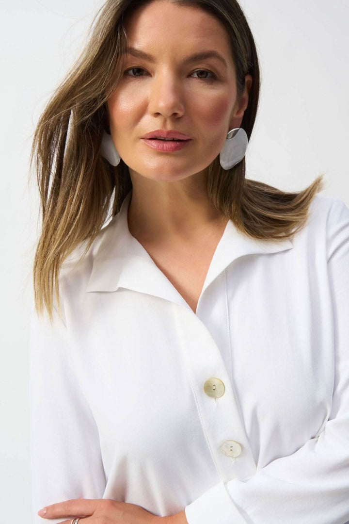 Femme portant une blouse classique blanche avec col en V et boutons, style élégant et léger.