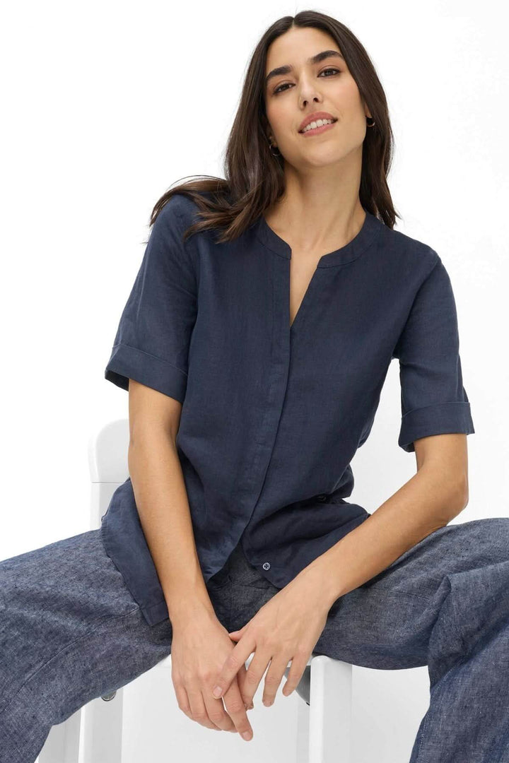 Femme portant une Blouse en lin VERI bleu avec encolure ouverte et manches courtes, idéale pour un look moderne et confortable.