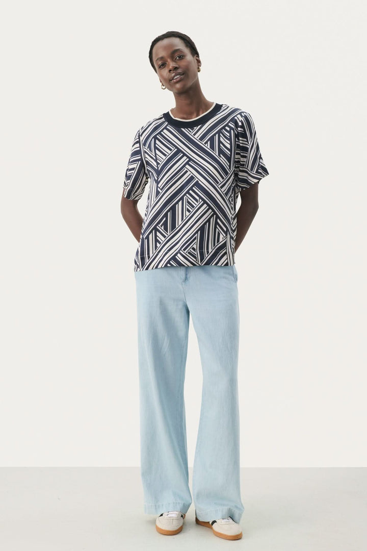 Femme portant un t-shirt à motif géométrique et un pantalon léger en denim, élégant et décontracté.