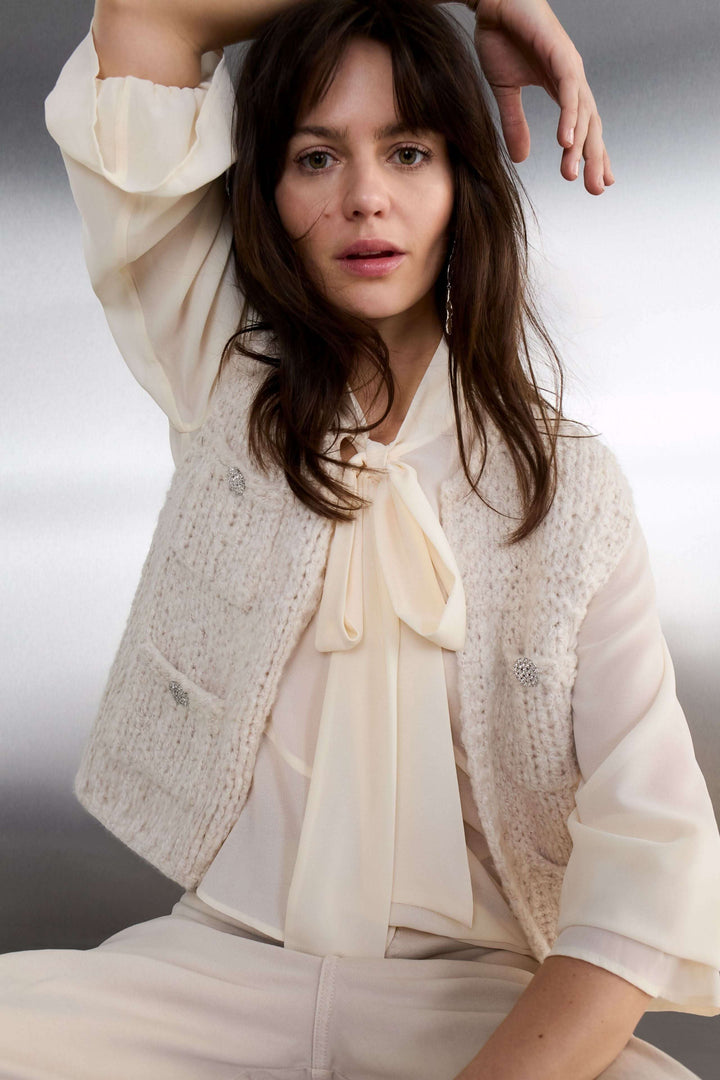 Modèle portant une blouse fluide à cravate col noué, élégante et raffinée, avec un gilet texturé. Tenue chic idéale pour le bureau.
