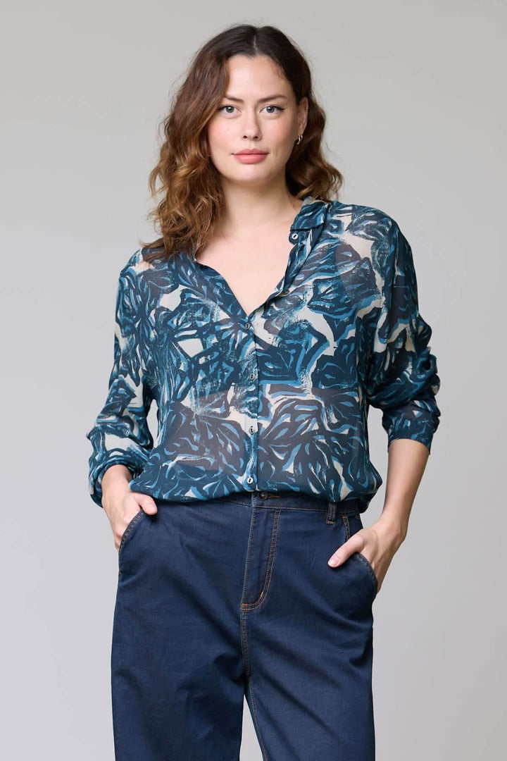 Femme portant une blouse fluide à imprimé abstrait avec manches longues, col ouvert et tissu léger, idéale pour le bureau ou sorties.