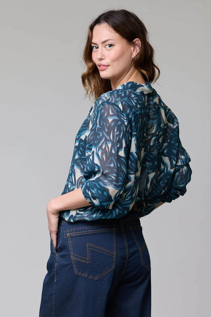 Femme portant une blouse fluide à imprimé abstrait avec manches longues et tissu léger, vue arrière.