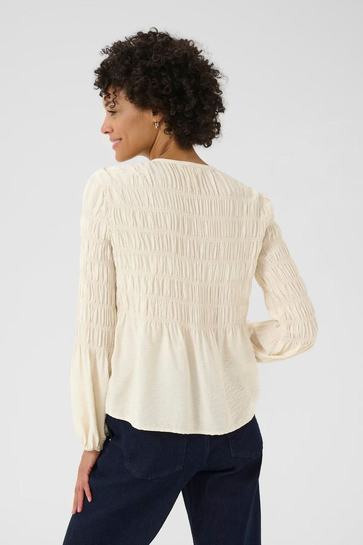 Femme portant une blouse à fronces écrue avec encolure ronde et patte boutonnée, vue de dos, style décontracté et féminin.