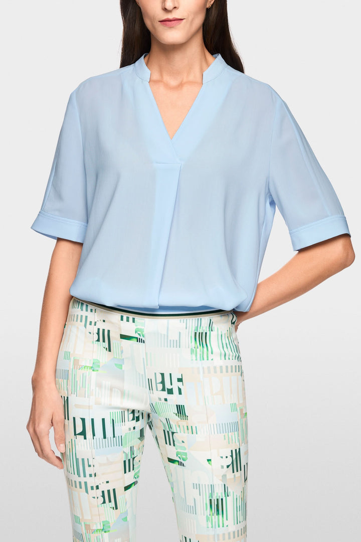 Blouse à manches courtes en tissu léger avec encolure en V, coupe droite fluide, manches à revers et pli central.