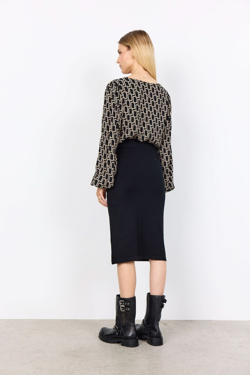 Blouse à motif graphique, silhouette fluide, manches bouffantes, portée avec une jupe noire et des bottes.