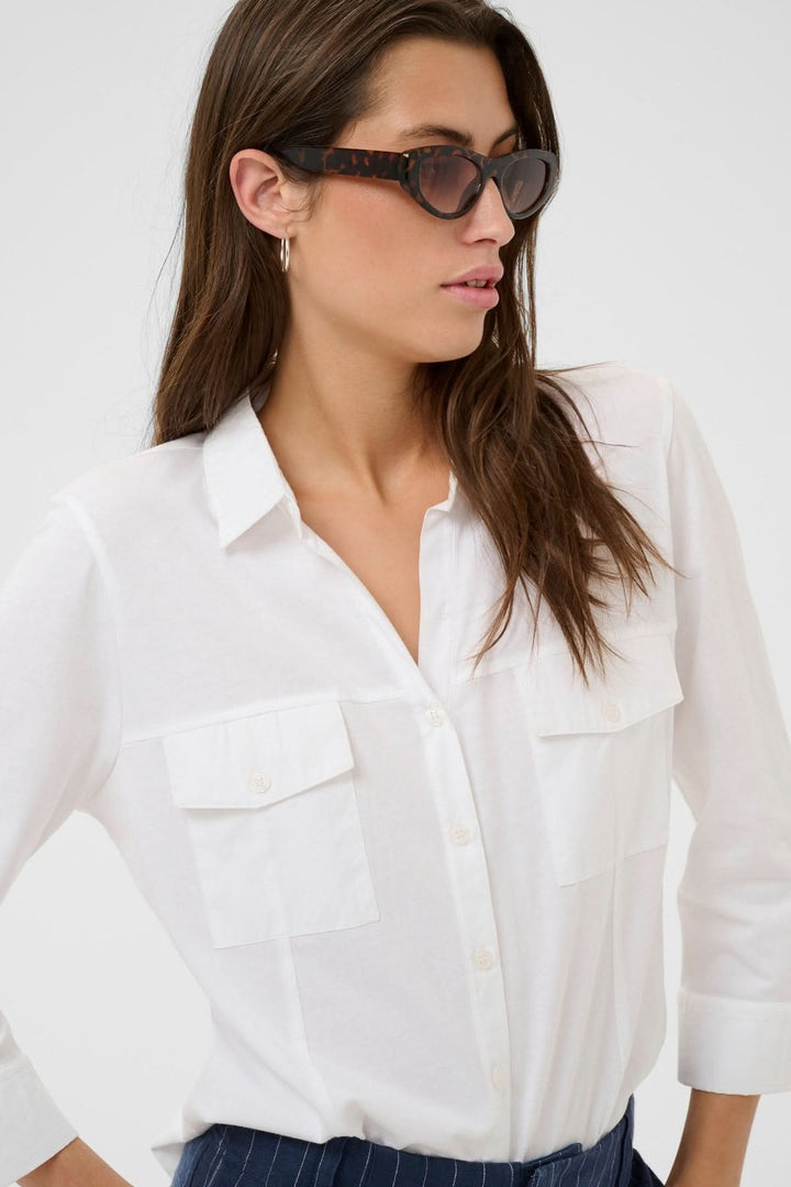Femme portant la blouse à poches utilitaires Anise, style fluide et contemporain, col chemise et fermeture boutonnée frontale.