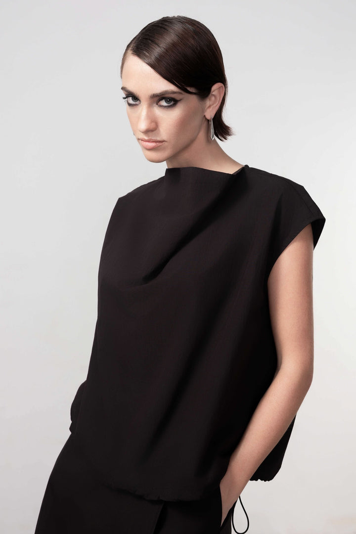 Femme portant une blouse sans manches avec un design épuré et un drapé subtil, idéale pour un look minimaliste et sophistiqué.