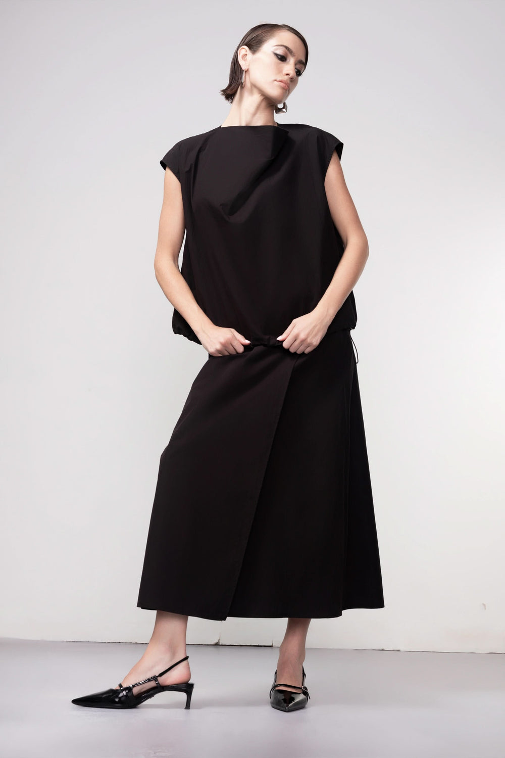 Femme portant une blouse sans manches noire avec un design épuré et élégant, idéale pour une tenue moderne et sophistiquée.