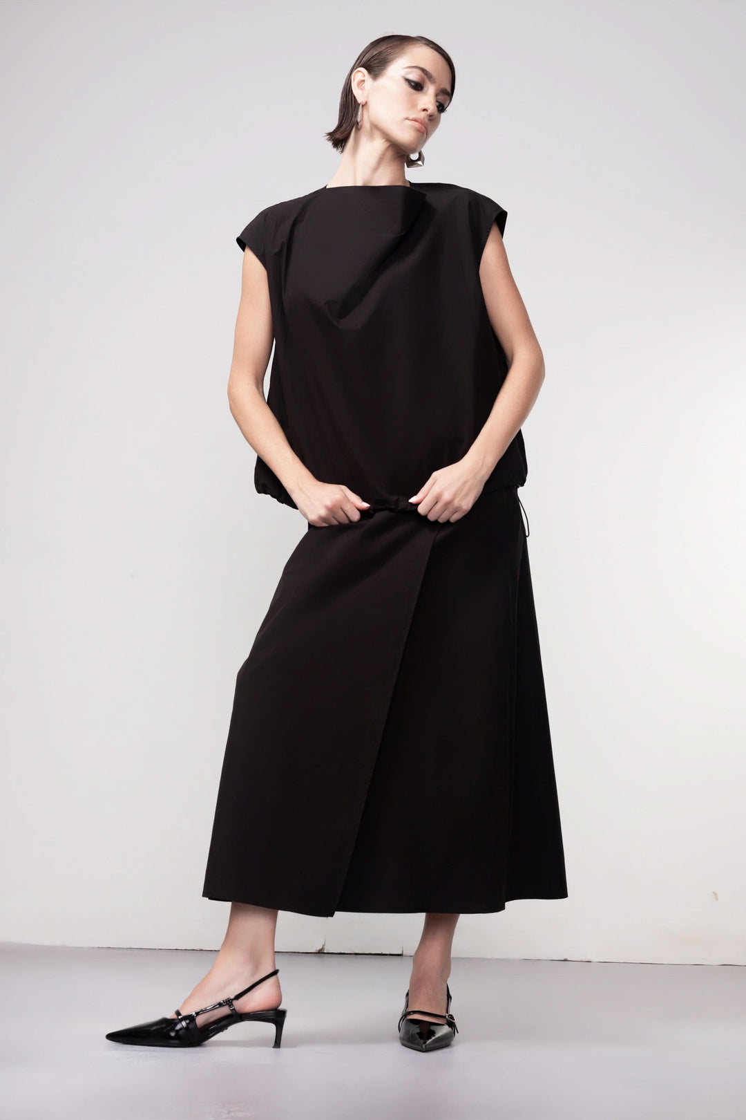 Femme portant une blouse sans manches noire avec un design épuré et élégant, idéale pour une tenue moderne et sophistiquée.