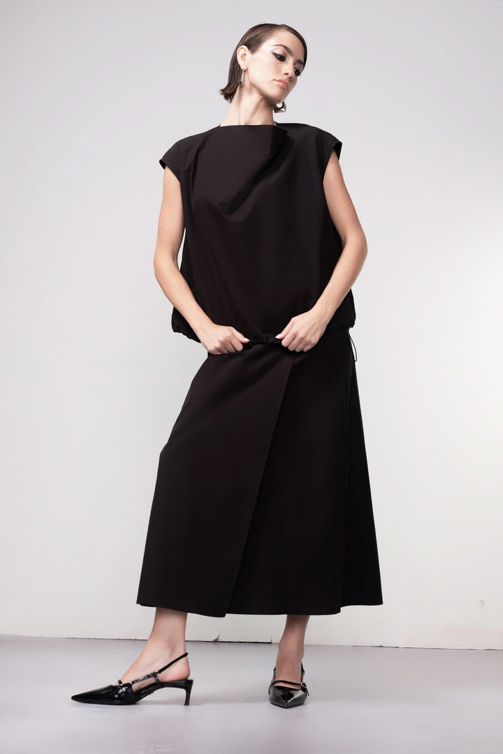 Femme portant une blouse sans manches noire avec un design épuré et élégant, idéale pour une tenue moderne et sophistiquée.