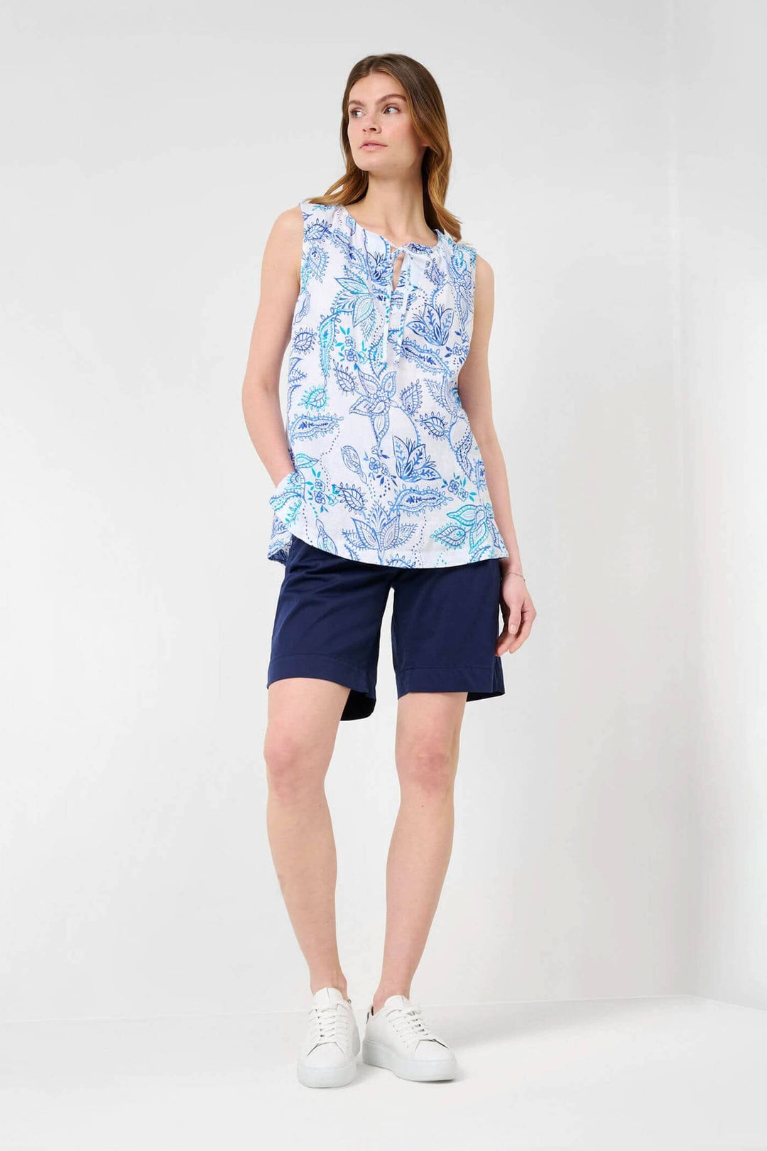 Blouse sans manches Vita en lin blanc avec imprimé floral, portée avec un short bleu marine.