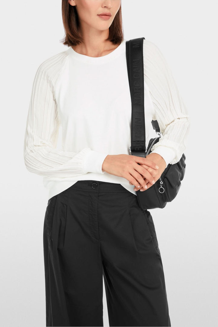 Femme portant une blouse unie blanche avec manches plissées, styling décontracté avec un sac noir.