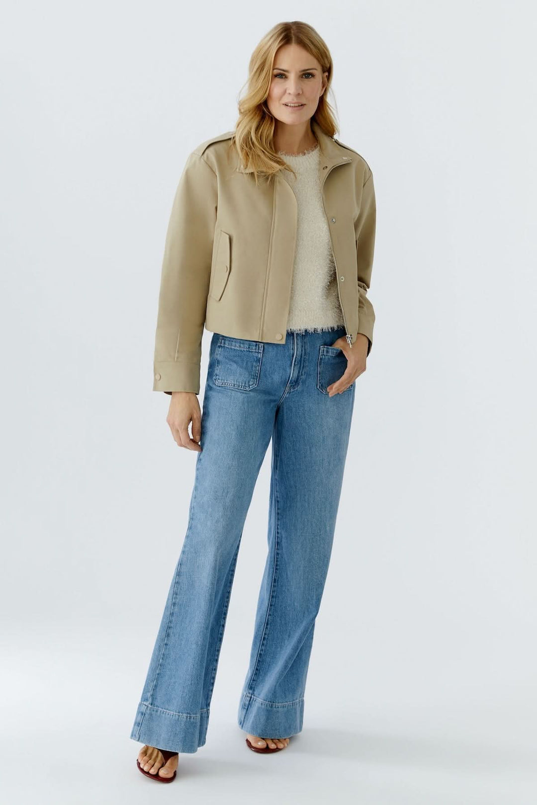 Femme portant un blouson court à col montant structuré beige avec un jean évasé, style moderne et décontracté.