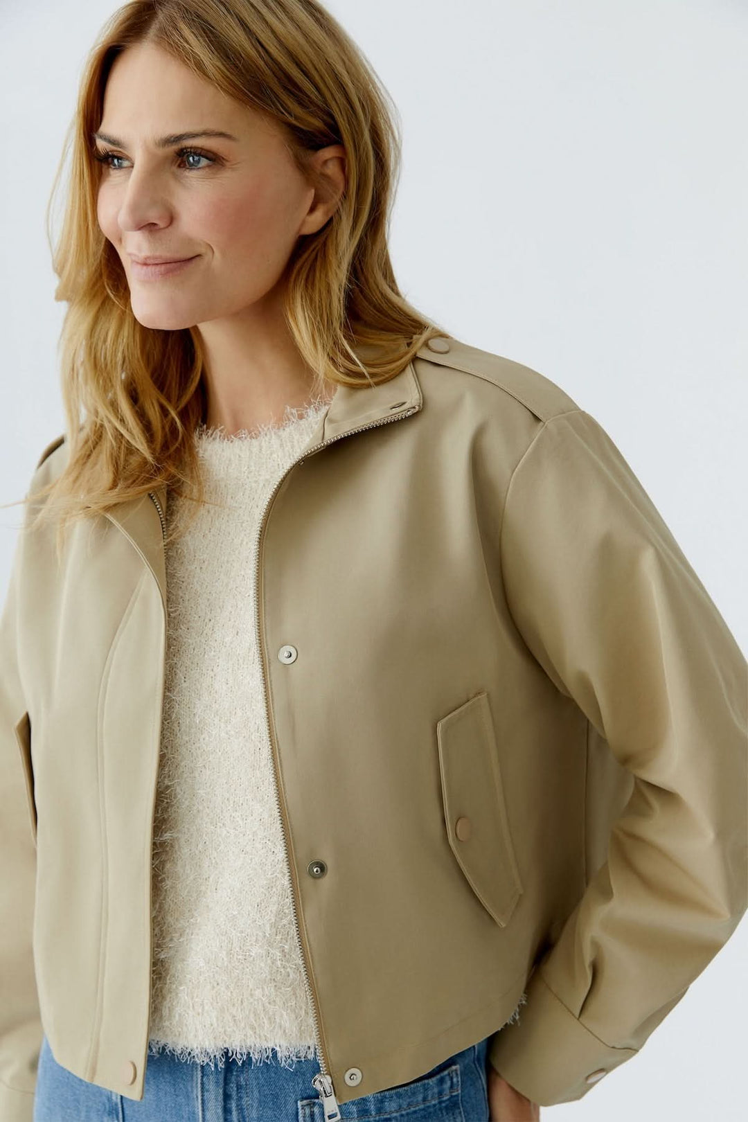Femme portant un blouson court à col montant structuré beige, idéal pour un look moderne et confortable avec un design épuré.