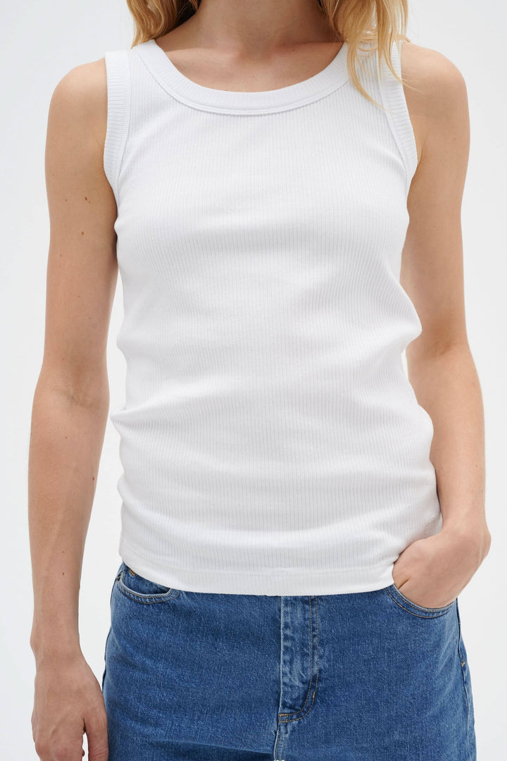 Camisole Dagna blanche, ajustée en coton côtelé, avec encolure ronde et bretelles larges, portée avec une jupe en denim.
