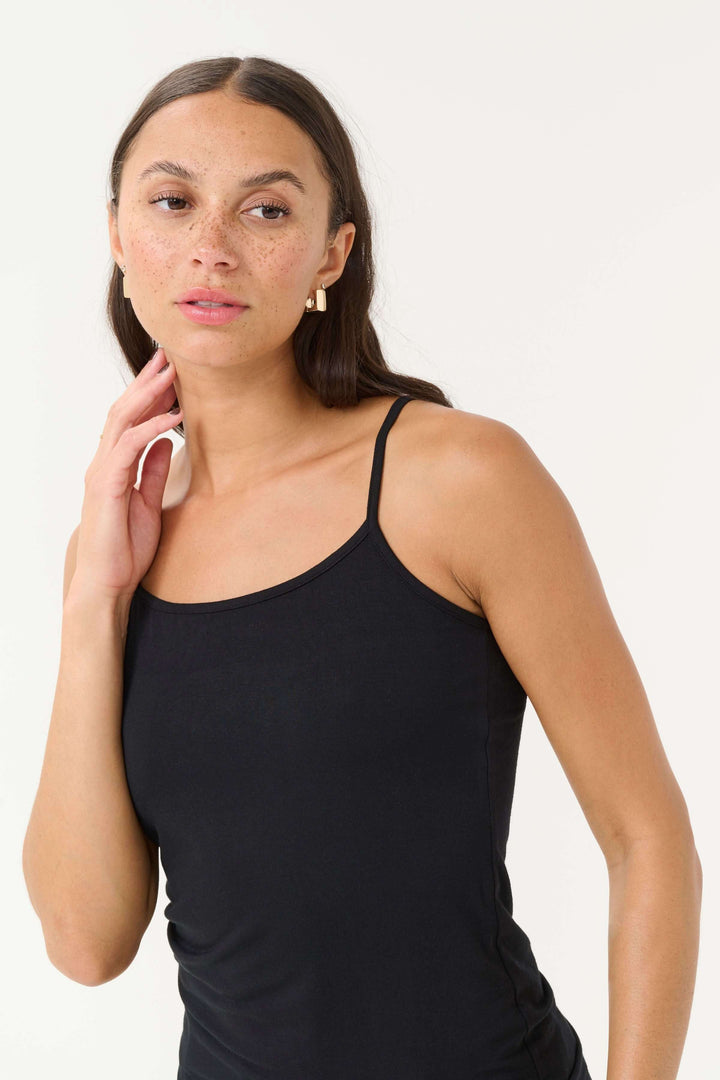 Femme portant une camisole Frida noire à bretelles réglables, offrant un look élégant et confortable.