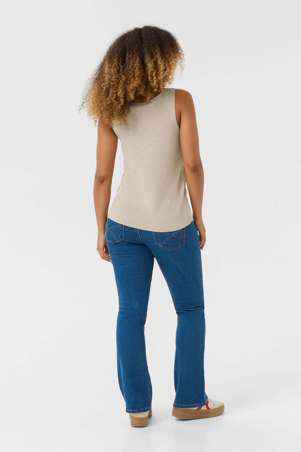 Femme vue de dos portant un débardeur en maille fine beige et un jean bleu, affichant un look décontracté.