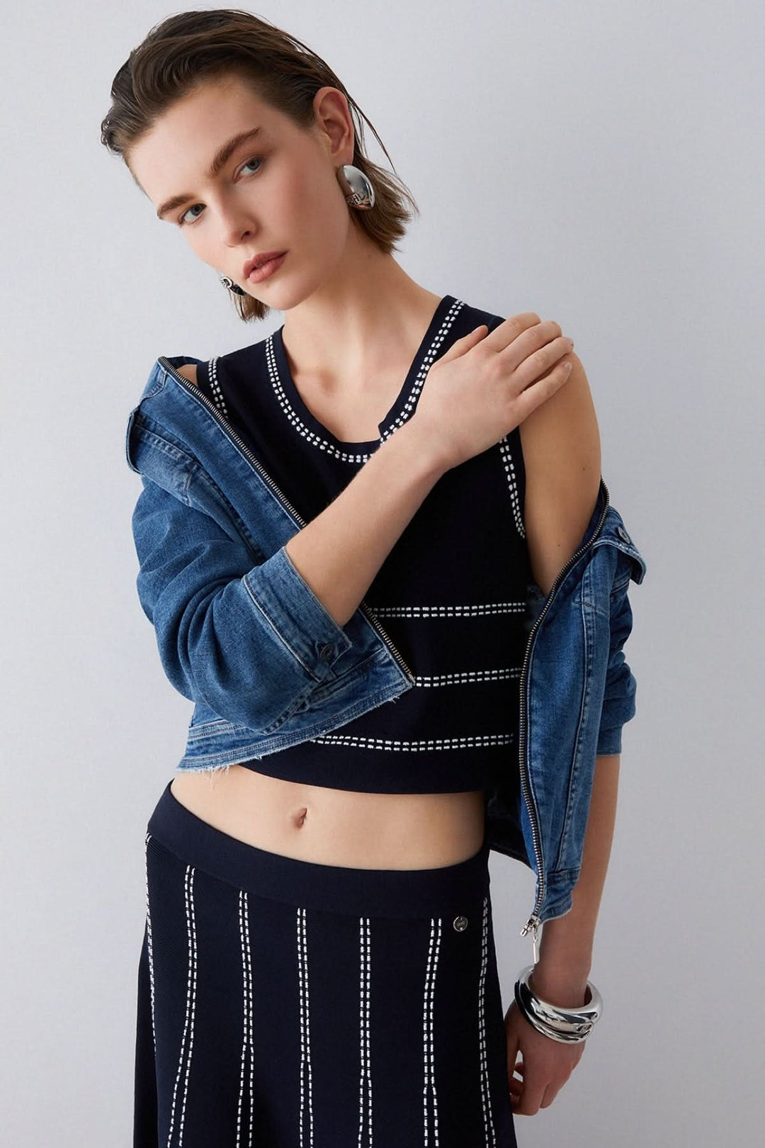 Femme portant une camisole en maille sans manches à motif rayé avec une veste en jean, tenant le col de la veste d&