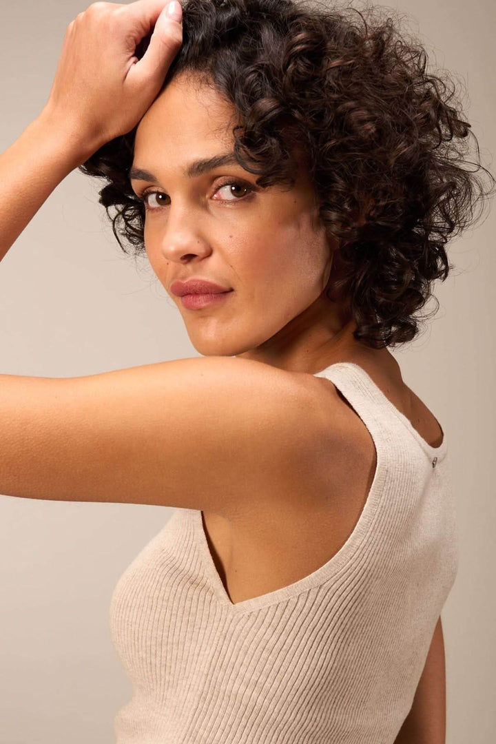Femme avec cheveux bouclés portant une camisole beige à encolure carrée, mettant en valeur son style élégant.
