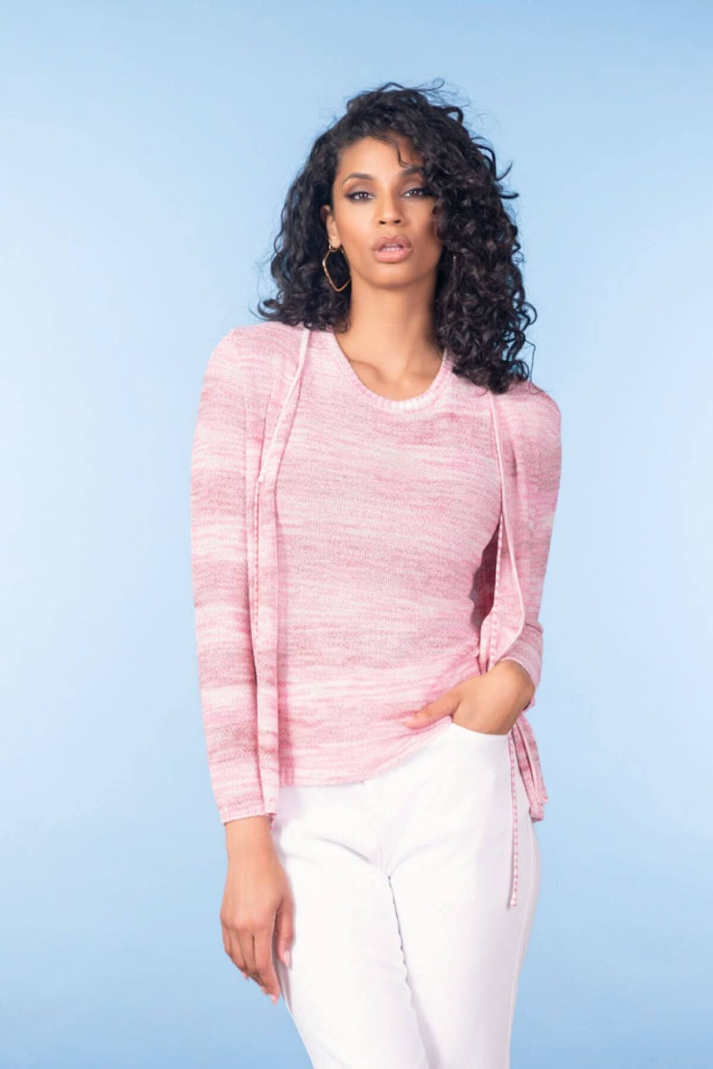 Femme portant un pull texturé rose avec manches longues sur fond bleu clair.