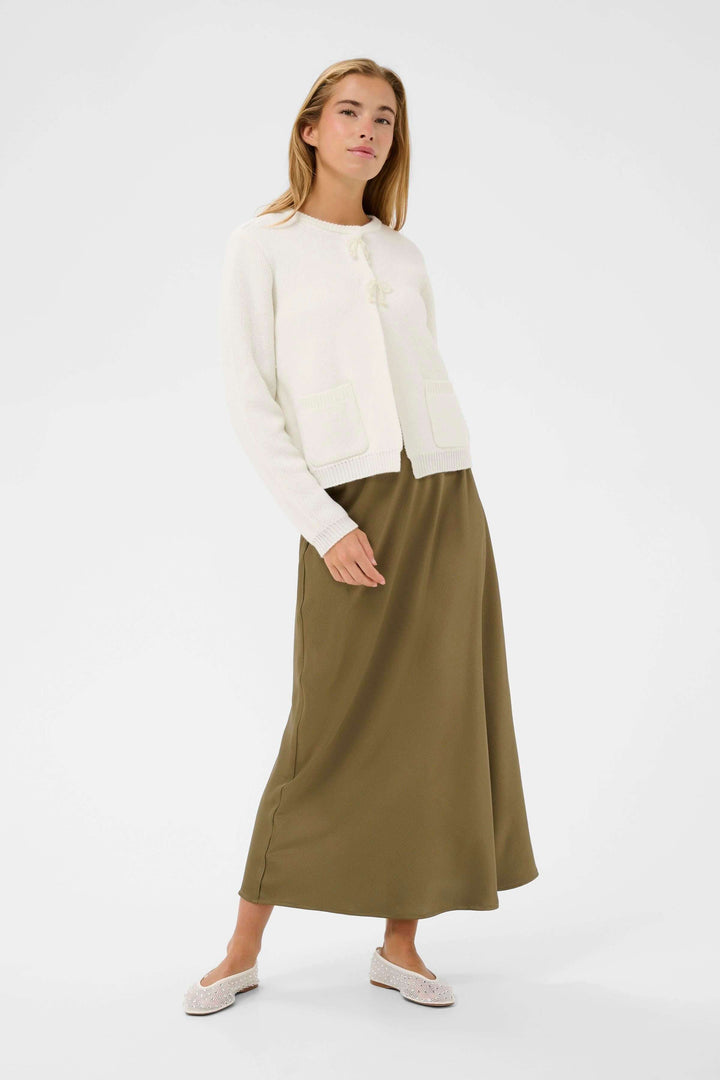 Cardigan Bowie blanc, style délicat et intemporel, porté avec une jupe longue pour un look quotidien élégant et féminin.