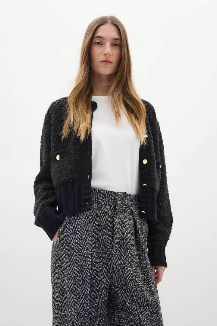 Cardigan Guo noir avec boutons dorés, maille texturée et coupe courte, porté par modèle en pantalon taille haute pour look chic.
