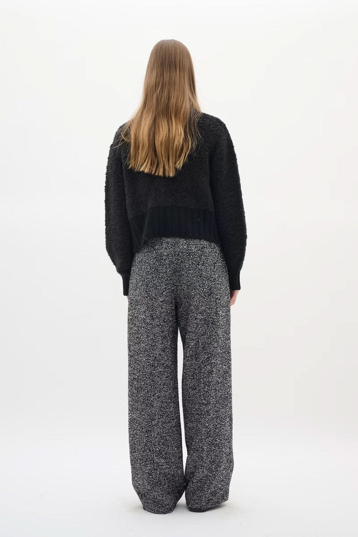 Person wearing Cardigan Guo, black textured knit with golden buttons, styled with high-waist pants for a chic silhouette from the back.