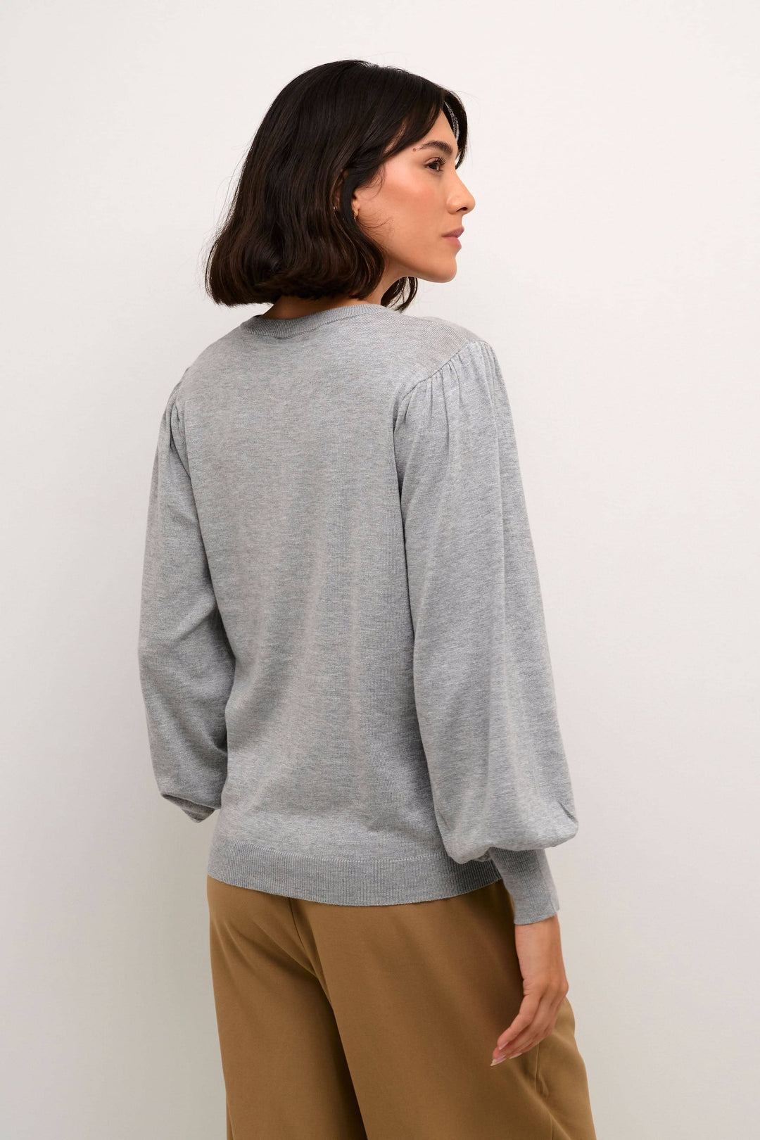 Femme portant un cardigan gris à manches ballons, vu de dos, avec un style classique et polyvalent.